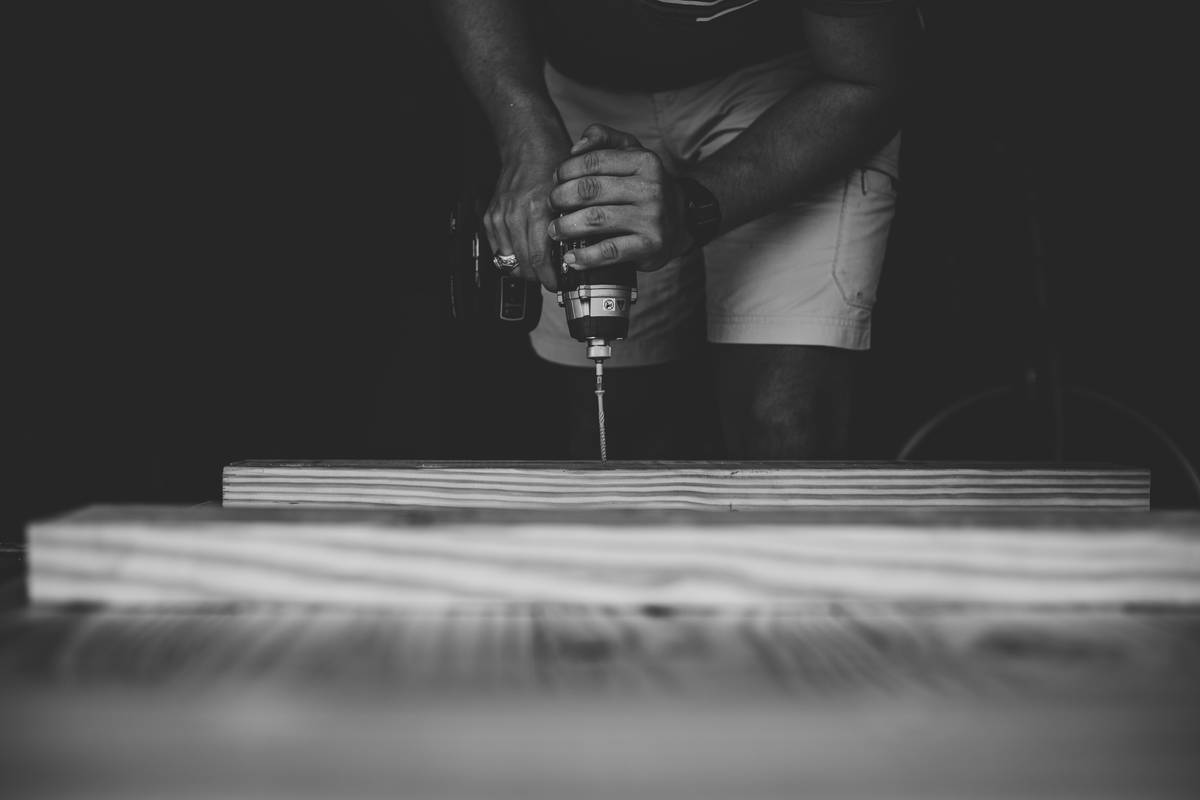 diy project power how to use: hands wearing gloves adjusting a cordless drill on a wooden workbench with clamps and safety goggles nearby